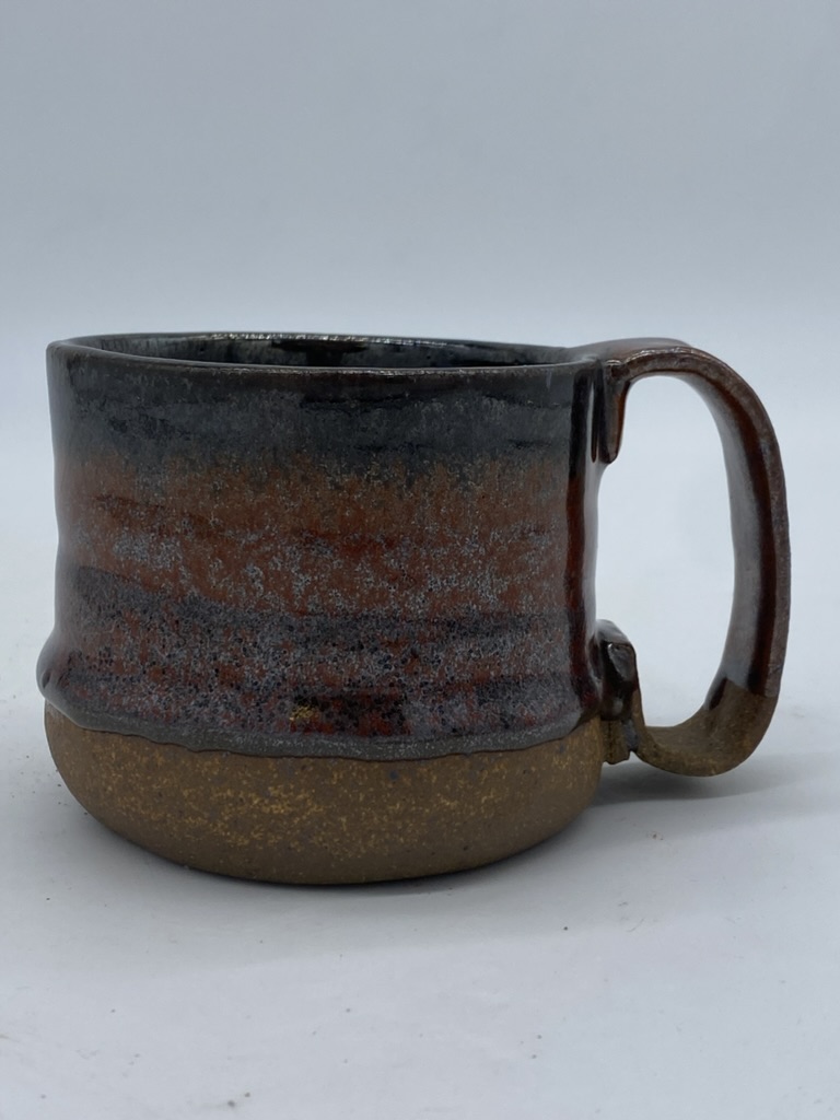 A medium-sized stoneware mug with a drippy red-black glaze and a rustic appearance.