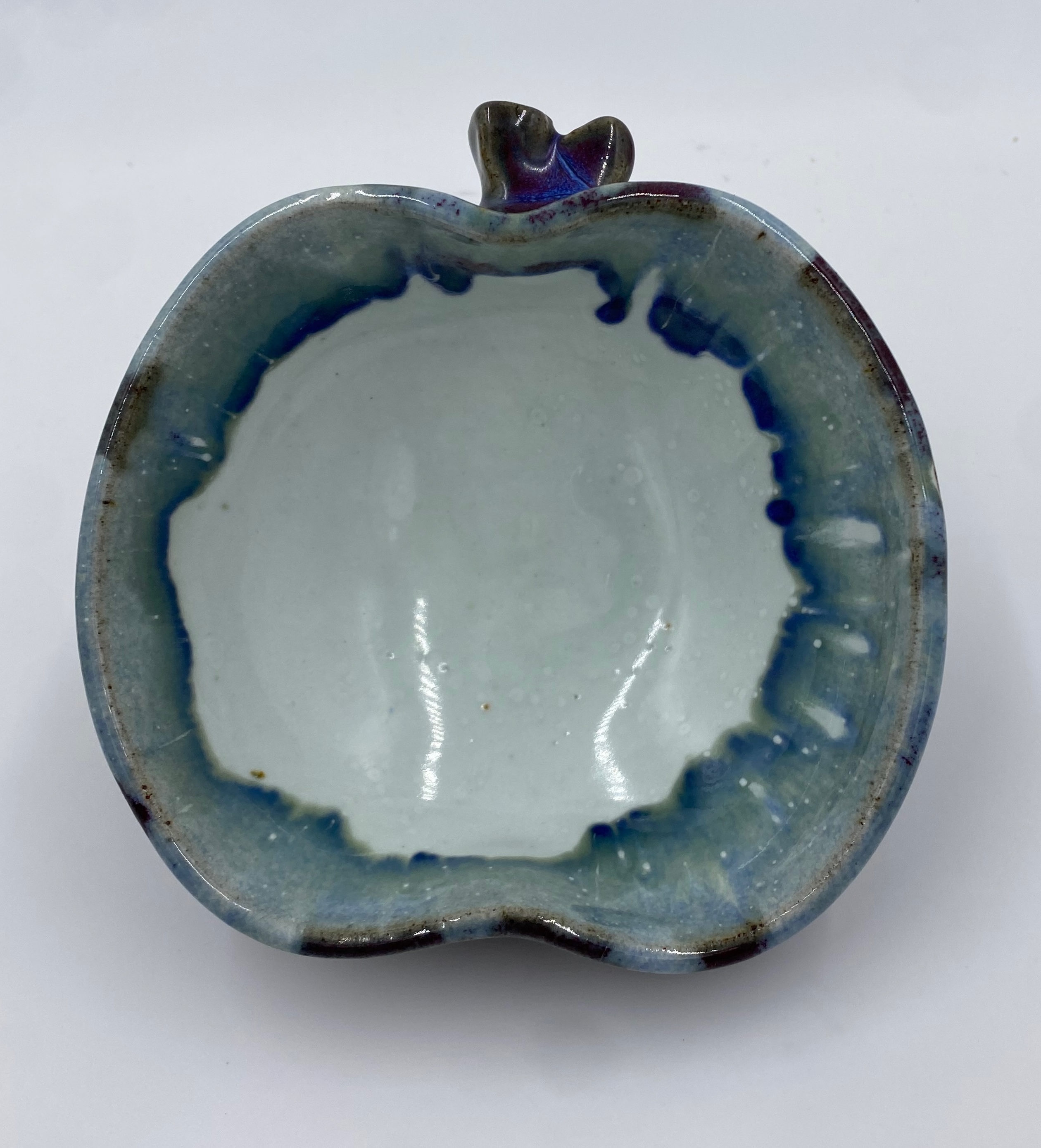 The inside of an apple-shaped bowl with a white glaze and reddish-purple drips.