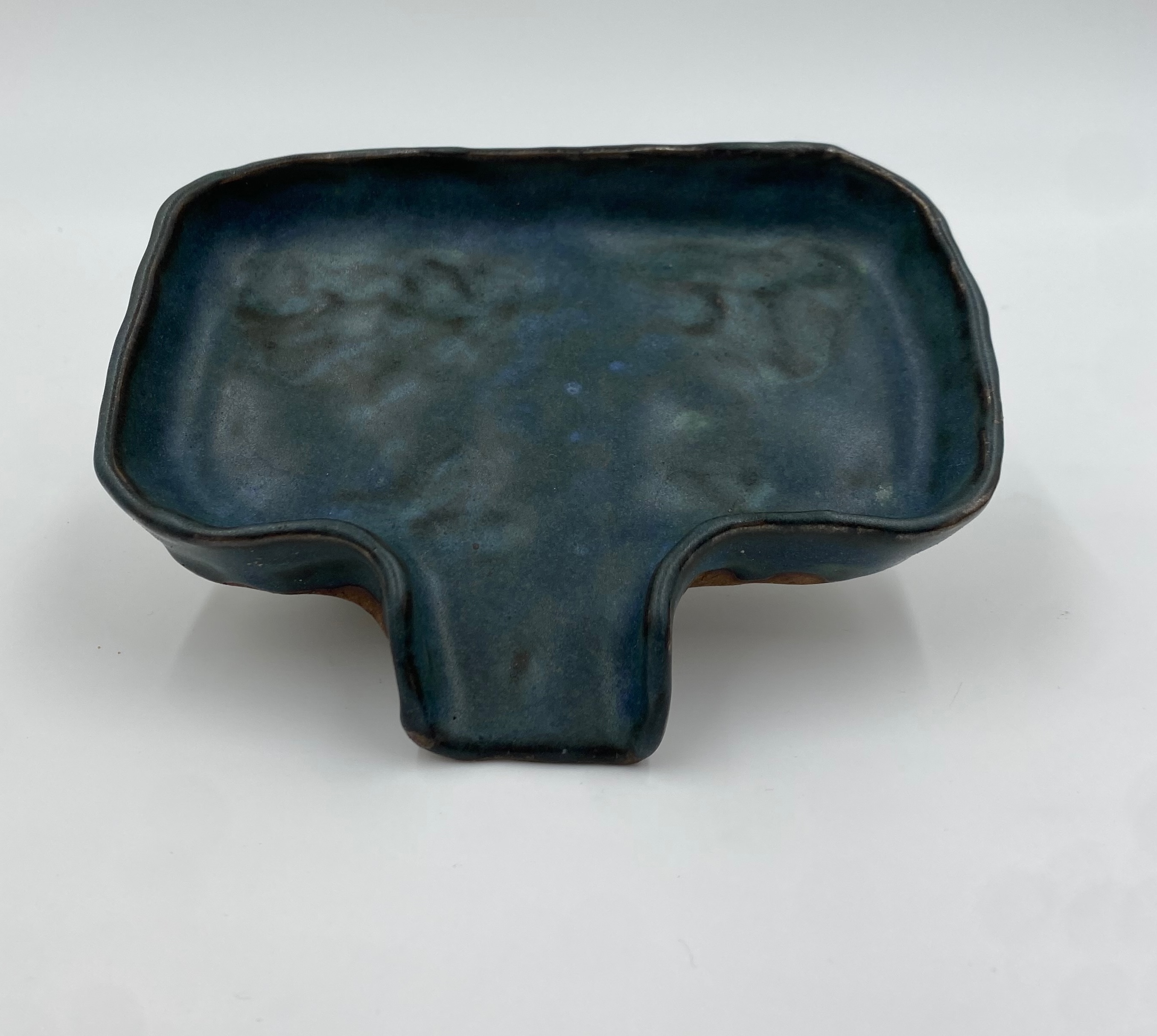 A green-black pinched soap dish with a sloped section that drains into the sink.
