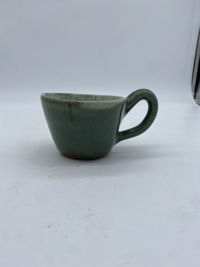 A large green stoneware teacup with a playful handle and a white interior.
